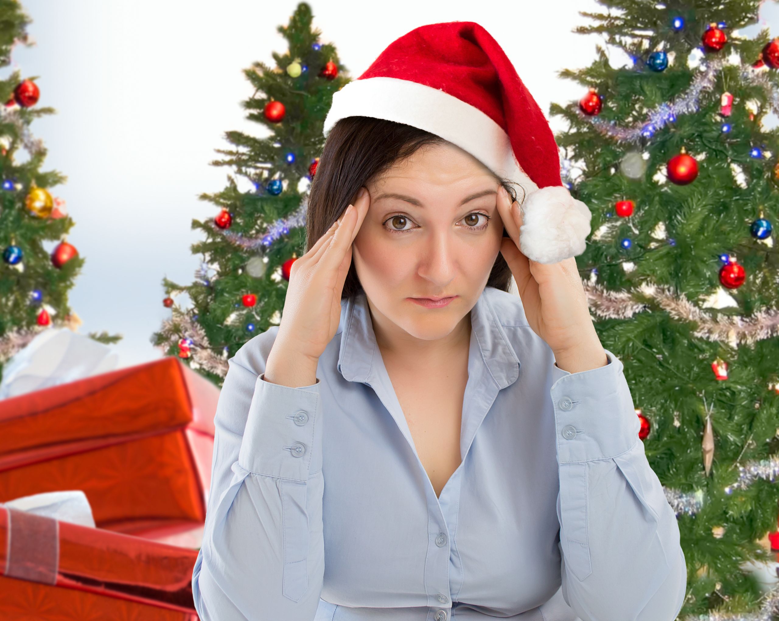 Stressed woman wearing a Santa hat with Christmas trees and gifts in the background